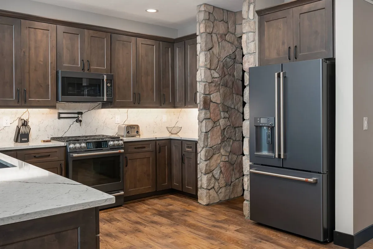 A stylish, modern kitchen with dark wooden cabinetry, stainless steel GE Café Series appliances, a natural stone wall, and a marble countertop. The space is designed for both culinary creativity and hosting, offering a cozy, contemporary vibe ideal for cooking and entertaining.