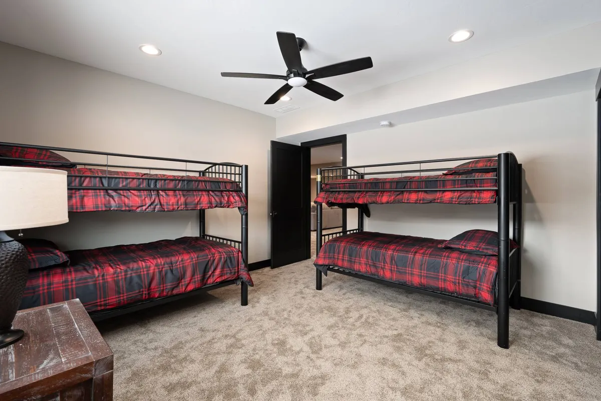 A playful and inviting bunk room with double bunk beds, ceiling fan, lamp, and carpeted flooring. The room is designed for group fun and relaxing nights, perfect for kids or extra guests.