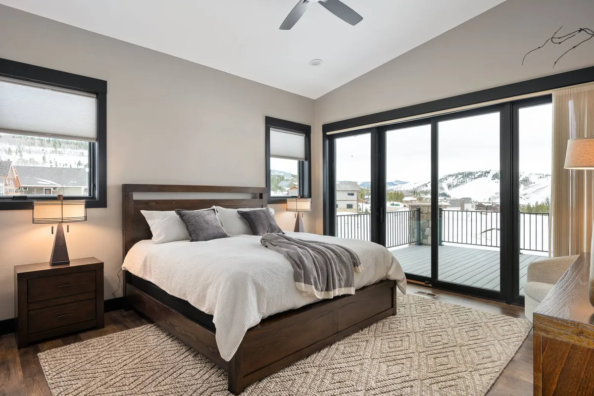 A serene bedroom with a cozy bed placed in front of large windows, flanked by nightstands. The room is bathed in natural light, inviting relaxation and peaceful mornings spent enjoying the view.