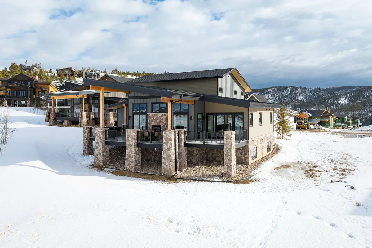 A modern mountain home surrounded by a pristine, snow-covered landscape with breathtaking views of the nearby mountains. The architecture invites visitors to imagine returning from a day of skiing or snowboarding, relaxing on the porch, and soaking up the sunset over the peaks.