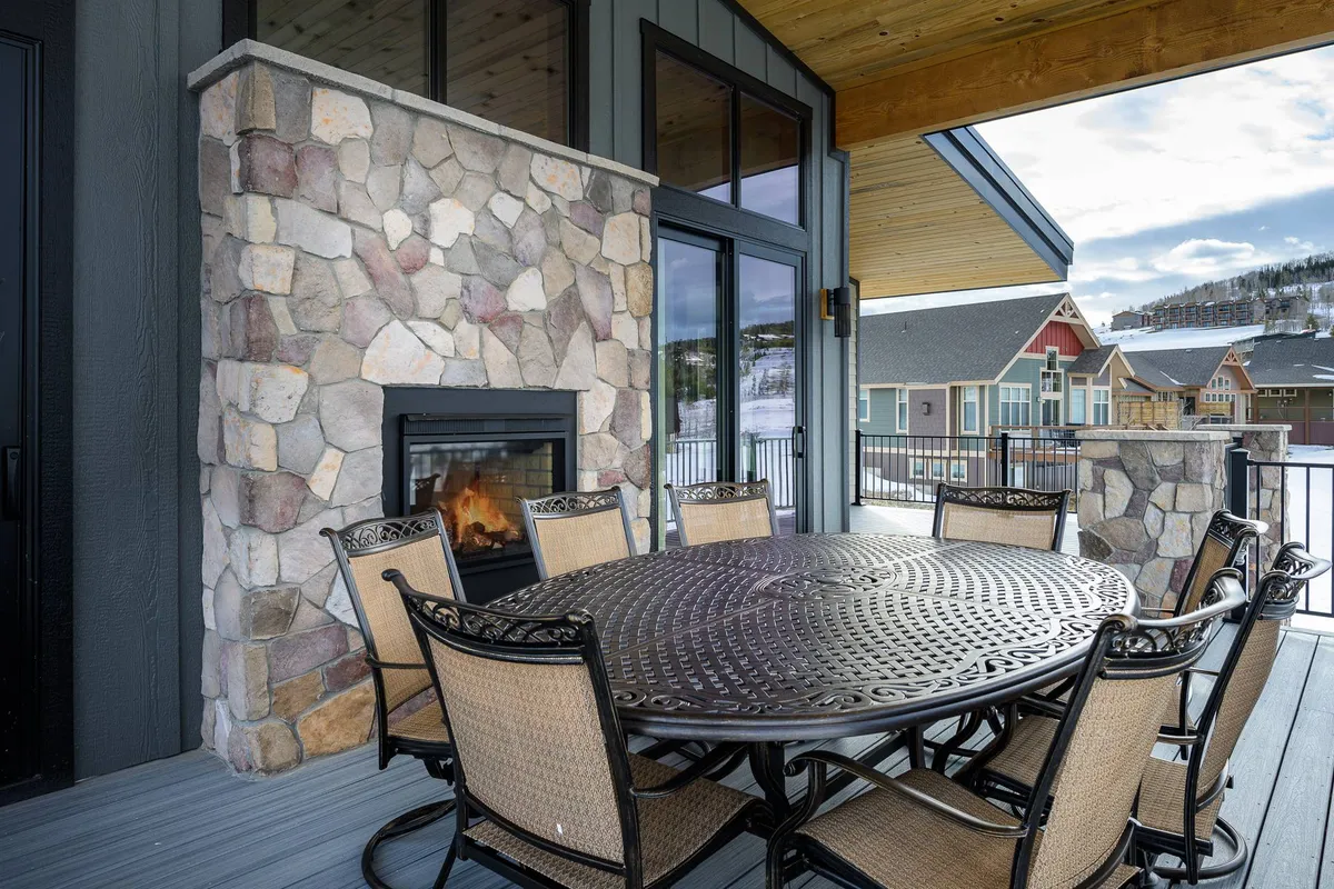 A cozy outdoor living space featuring a stone fireplace, a circular dining table, and comfortable seating. The setup suggests warmth and sociability, ideal for gathering with friends or family, and is positioned to enjoy the fresh mountain air.