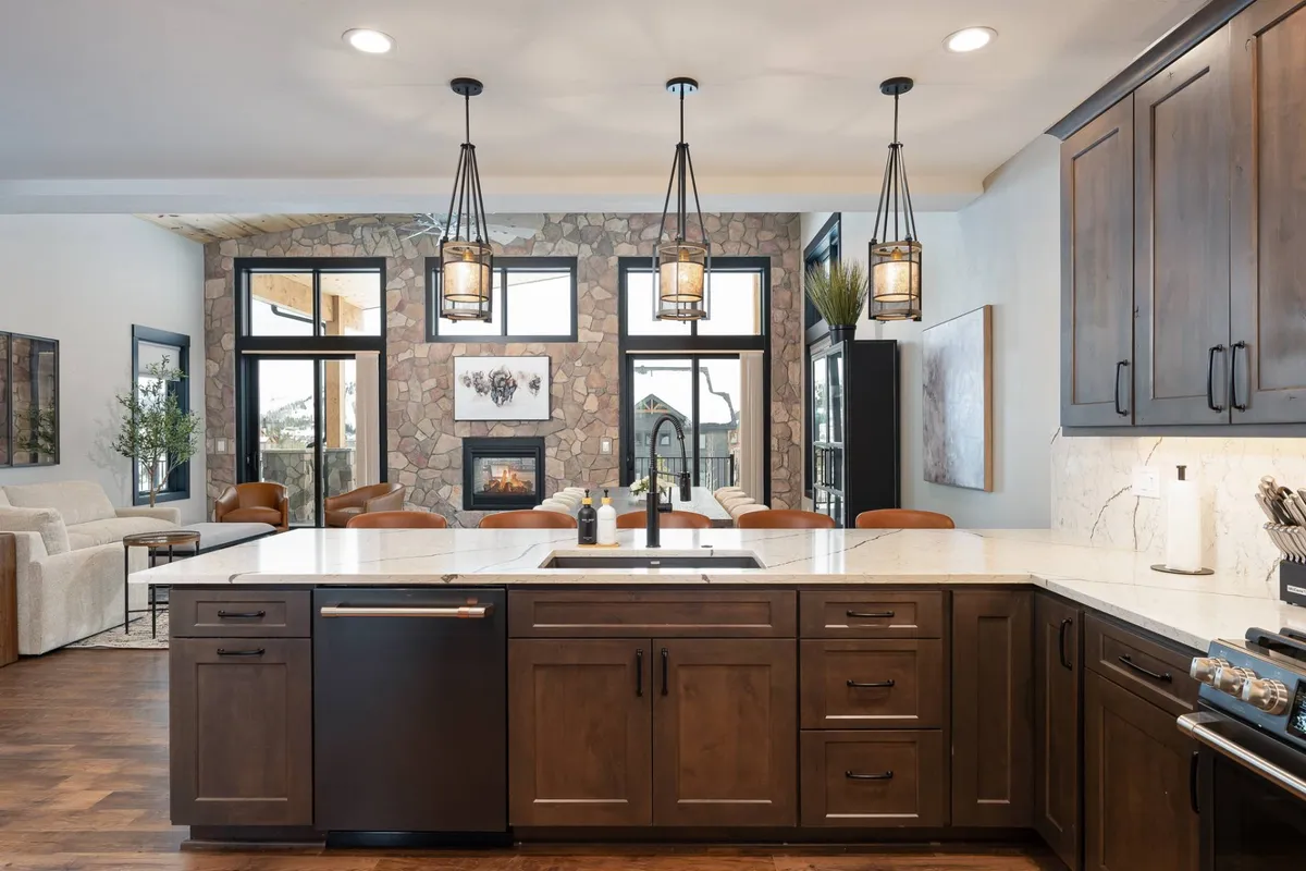 This image depicts a welcoming open-concept kitchen with a striking stone feature wall, a spacious kitchen island surrounded by seating, elegant lighting fixtures, and a cozy dining area. The setting is ideal for gatherings, entertaining, and shared meals, emphasizing the social and comfortable aspects of the home.