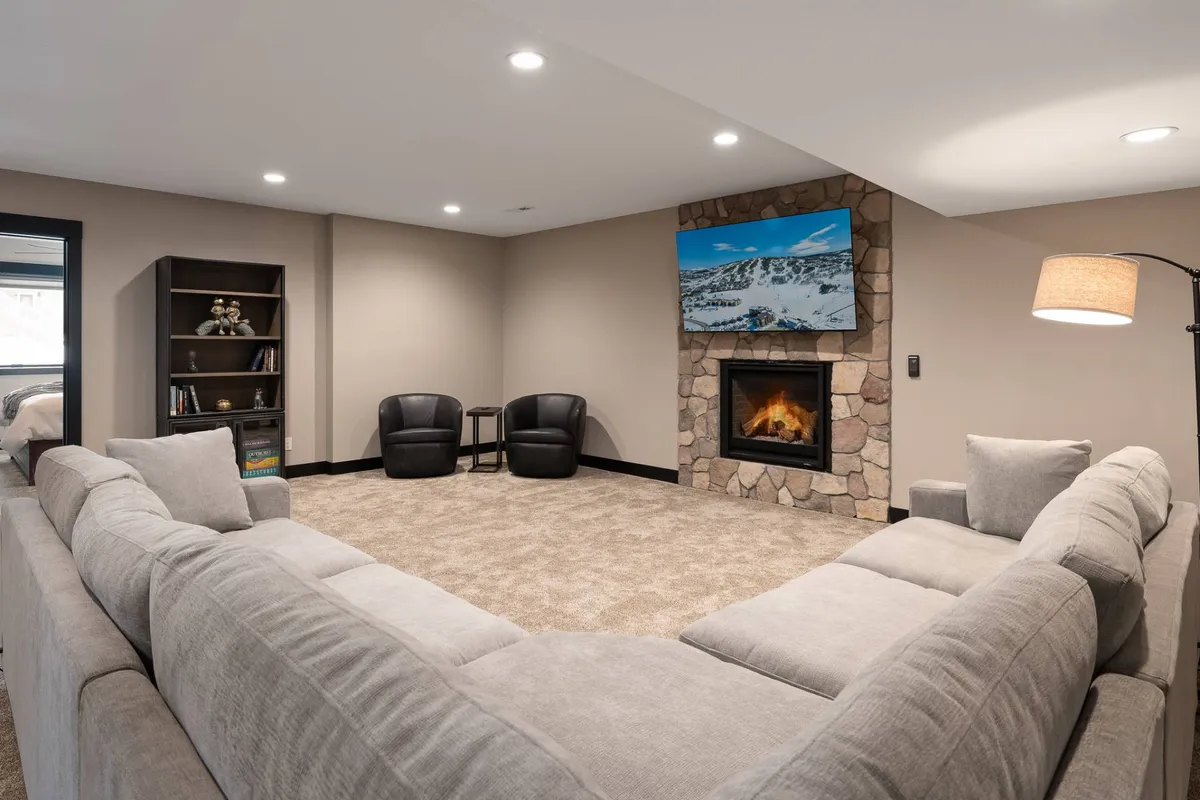 A comfortable living area featuring a large sectional sofa, a stone fireplace, a television, and a well-stocked bookshelf. The arrangement encourages relaxation and socializing, ideal for movie nights or intimate evening chats after dinner.