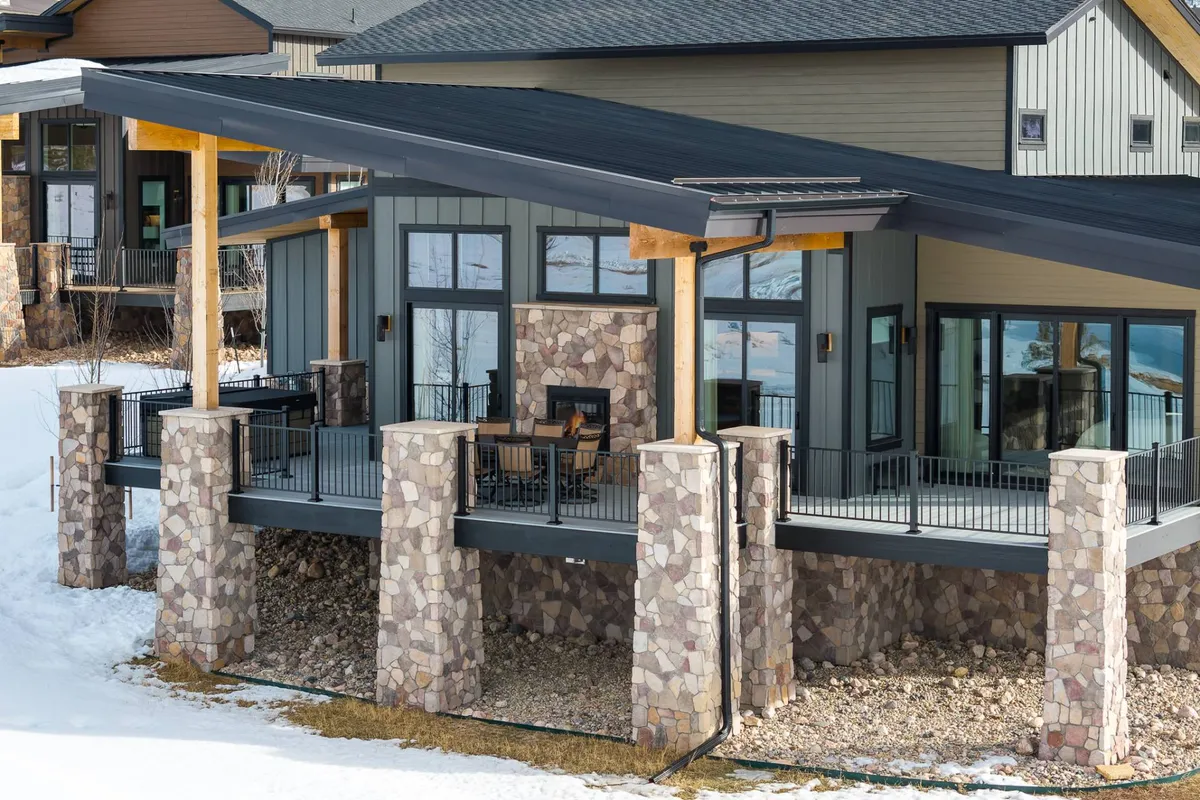 An exterior view of the patio area, framed by large stone pillars and expansive windows, with outdoor seating oriented to take in sweeping mountain vistas. The mood is tranquil and inviting—an ideal transition to the hot tub deck and outdoor relaxation.
