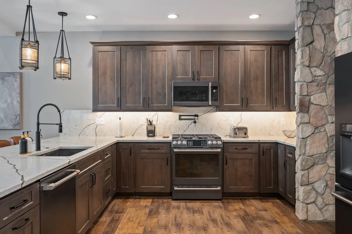 A stylish kitchen scene with dark wooden cabinets, a marble countertop, stainless steel appliances, and a stone wall accent. The space feels modern and cozy, emphasizing quality finishes and a layout conducive to both cooking and entertaining.