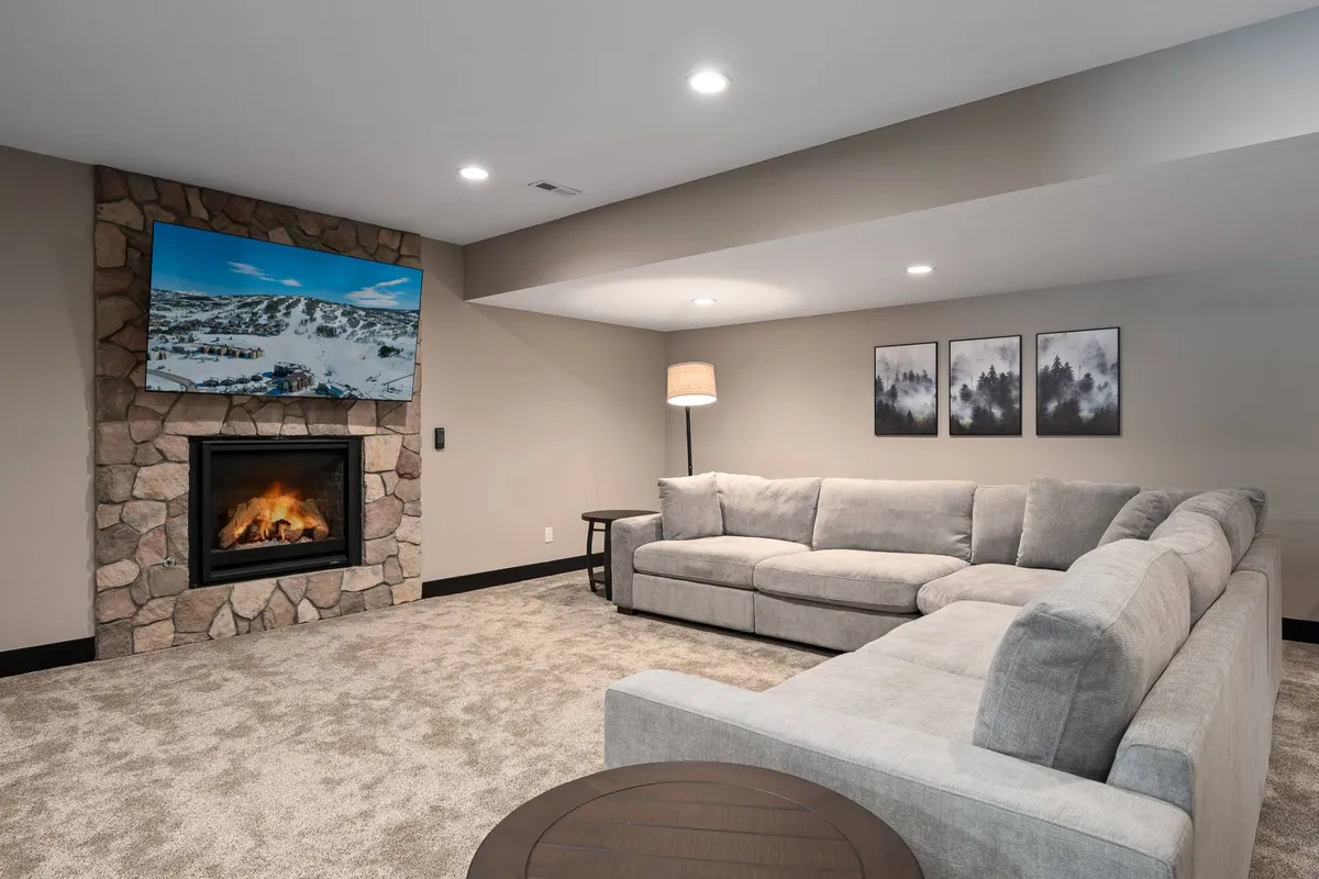 This inviting living area features a cozy sofa in front of a prominent fireplace, with a television and curated artwork framing the space. Warm lighting and comfortable seating evoke a sense of gathering and relaxation, ideal for socializing, watching movies, or enjoying fireside chats after a day outdoors.
