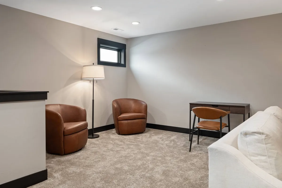 A cozy nook furnished with two brown leather armchairs and a small desk with a chair, adjacent to a light-colored sofa and a floor lamp. The arrangement creates a welcoming spot for reading, relaxing, or planning the next outdoor adventure, and the warm palette suggests a pet-friendly, inviting atmosphere.