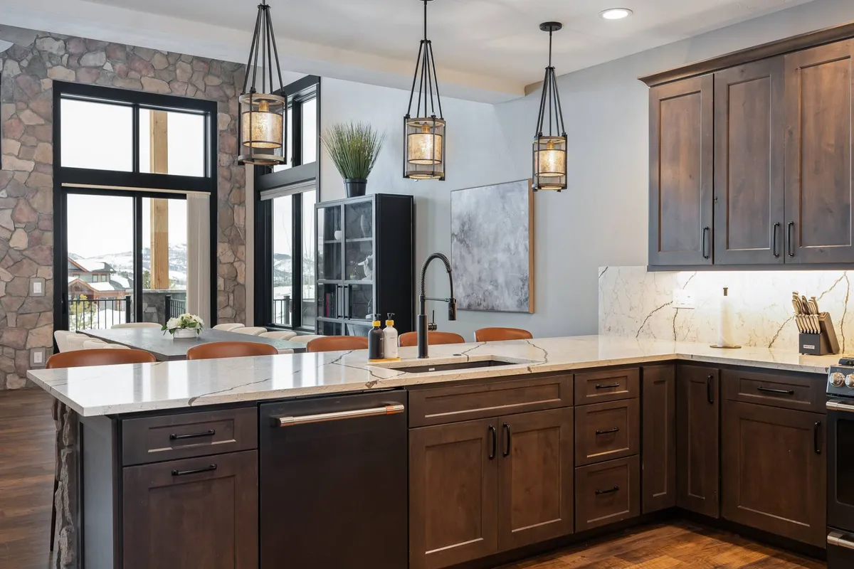 A bright, spacious kitchen with a large island, stylish pendant lighting, and a natural stone wall backdrop. The image captures an atmosphere perfect for cooking, entertaining, and creating memories—underscoring the idea of hosting family gatherings or celebrating milestones.