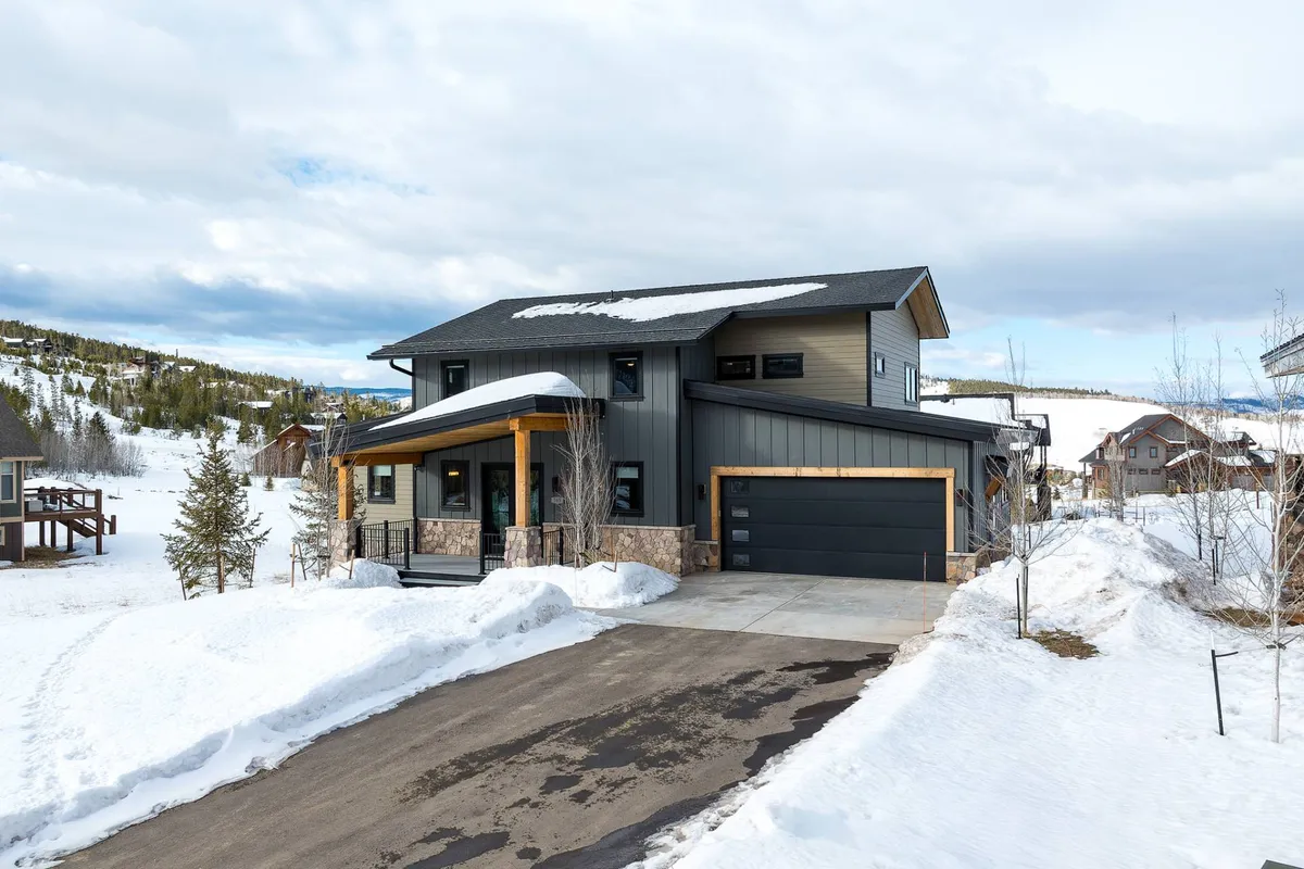 A front porch scene of the home featuring modern architectural details, wooden accents, and snow-blanketed ground. The view hints at the surrounding hills and the welcoming atmosphere for returning skiers or those ready for winter exploration.