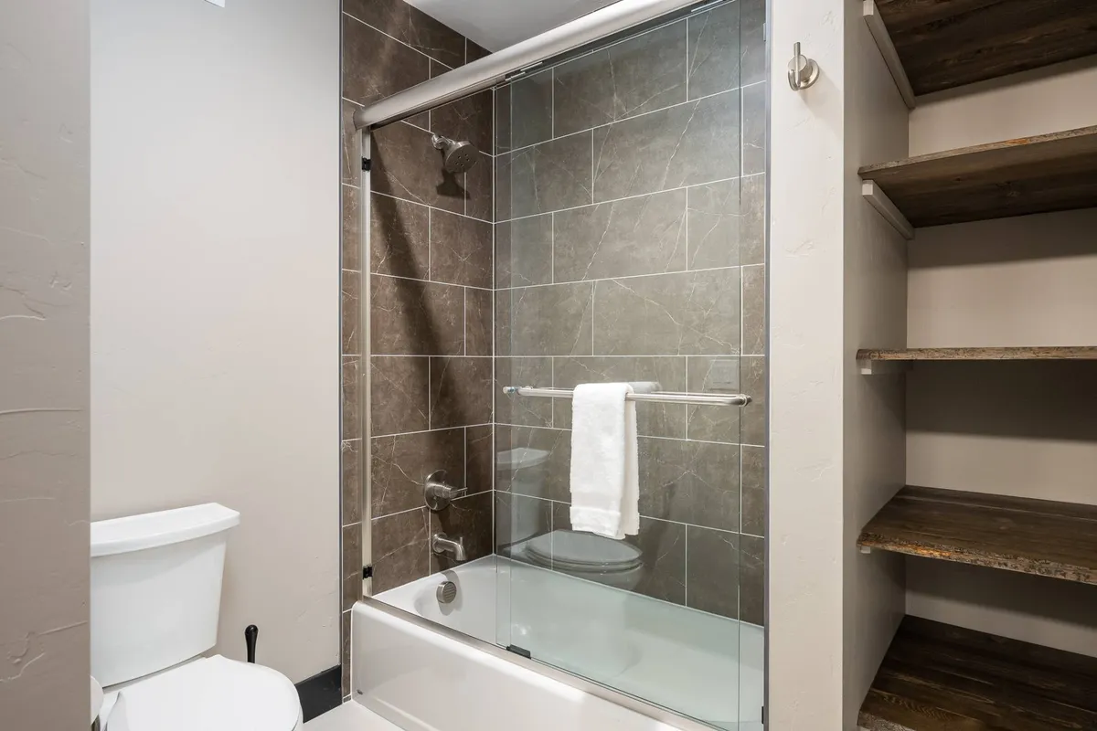 A luxurious spa-inspired bathroom featuring a glass shower enclosure, textured wall tiles, and wooden shelving for organized storage. The space feels refreshing and organized, echoing a true spa environment.