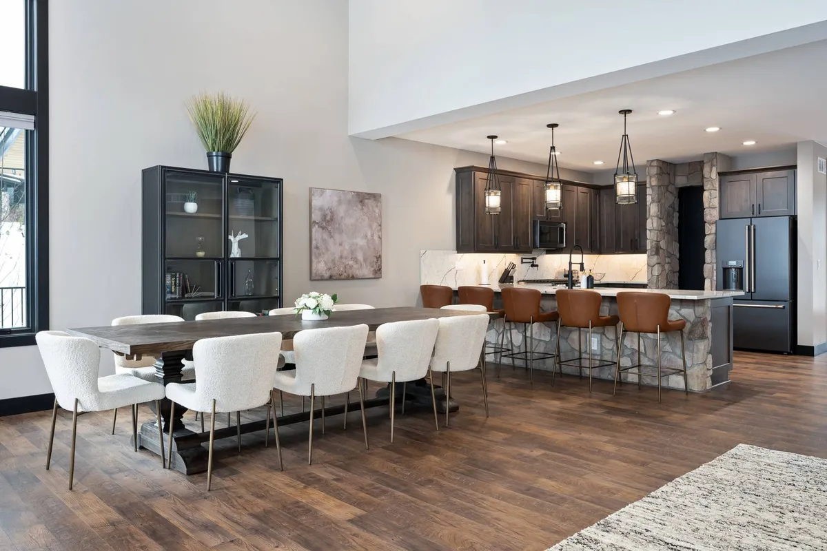 A welcoming open-concept space featuring a large dining table, a kitchen island with bar stools, and a decorative cabinet. The arrangement invites guests to gather, share meals, and socialize. The kitchen is visible and seamlessly blends with the dining area, emphasizing togetherness and hospitality.