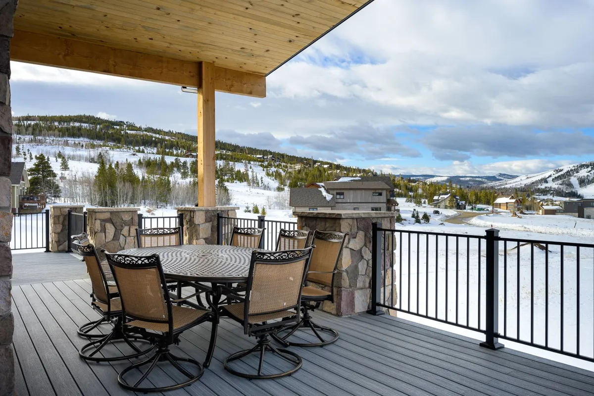 This image captures an outdoor dining table set on a deck or patio, surrounded by a stone railing and offering a sweeping view of the mountains in the distance. The seating arrangement is inviting, perfect for group gatherings, with the scenic backdrop underscoring the connection to nature and the outdoors.